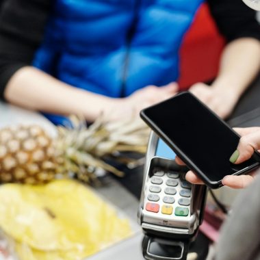 A customer uses a smartphone for contactless payment at a retail checkout with fresh produce.