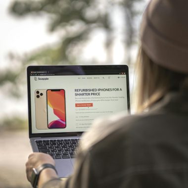 A woman using a laptop outdoors in Helsinki, Finland, viewing refurbished phone options.