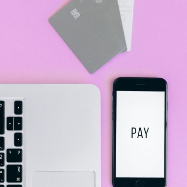 Top view of mobile payment setup with smartphone, credit cards, and laptop on pink background.